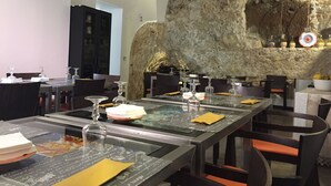 En restaurant med en stenvæg i baggrunden, borde dækket med glas og servietter, og et moderne interiør.