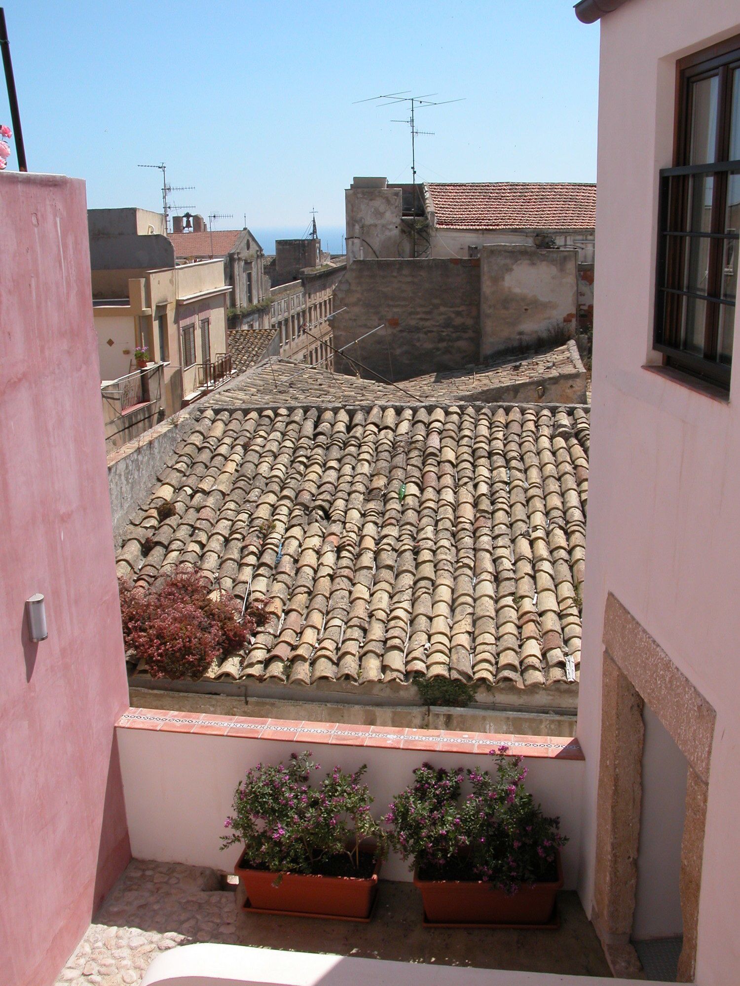 Eine Dachterrasse mit Terrakottafliesen, Topfpflanzen und freiem Blick auf die Stadtlandschaft.