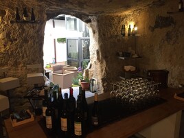 Una cantina vinicola rustica con parete in pietra, scaffali per vino e un’area bar con bicchieri e bottiglie.