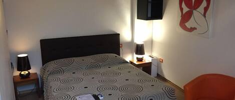 A bedroom with a bed, a nightstand, a lamp, a chair, and a wall art piece.