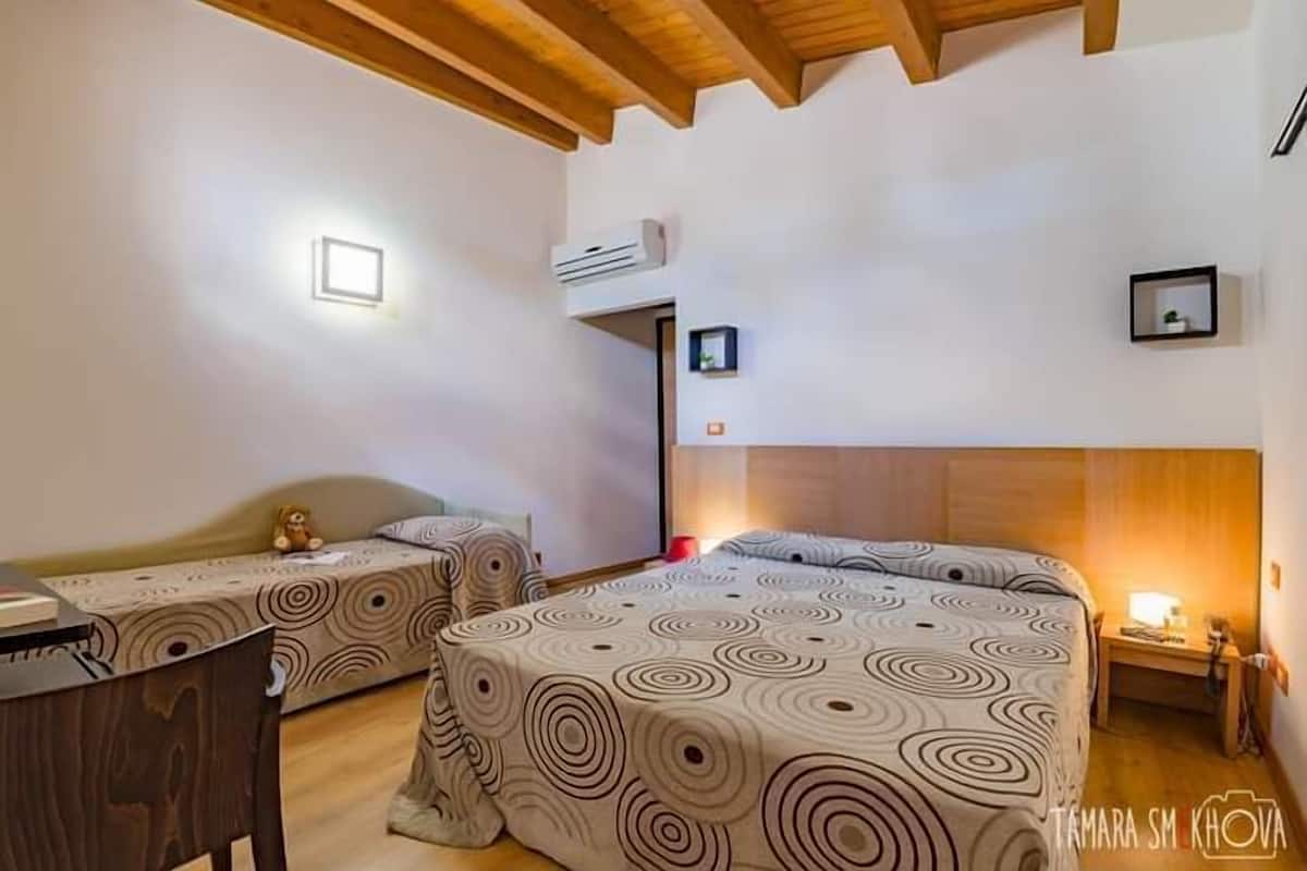 A bedroom with two beds, a wooden ceiling, a small desk, and a nightstand.