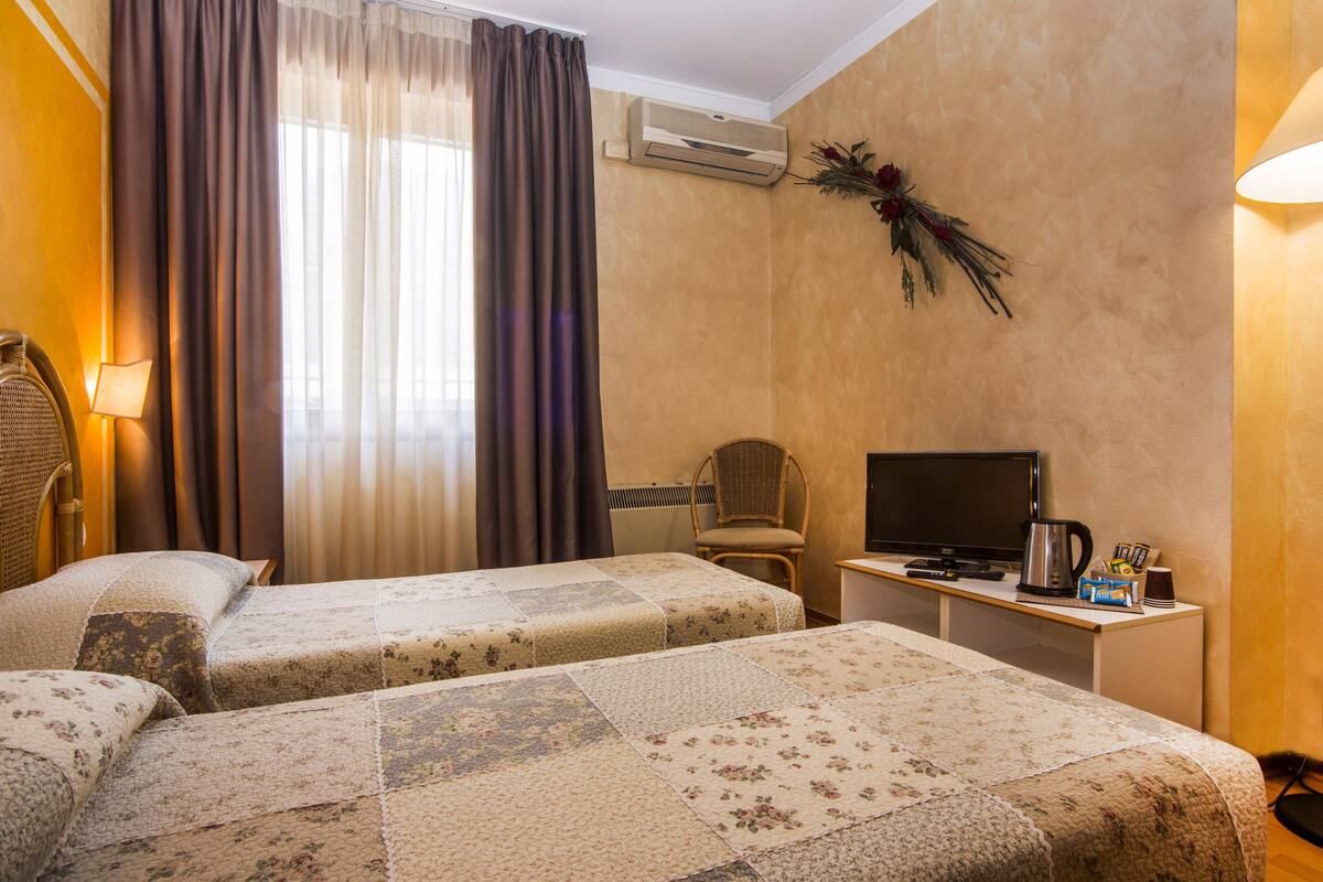 A hotel room with two beds, a television, a desk with a coffee maker, and a chair.