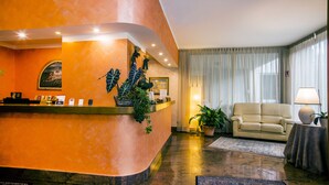 A hotel reception area with a curved orange wall, a reception desk, a beige sofa, and a potted plant. - Le Pageot (Aosta)
