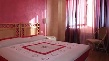 A hotel room with a large bed, a chair, a nightstand, and a window with curtains.