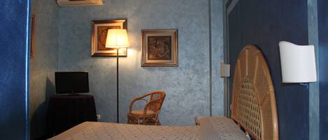 A bedroom with a bed, a television on a stand, a chair, and framed pictures on the wall.
