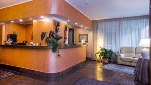 A reception area with a curved counter, a sofa, and a lamp. - Le Pageot (Aosta)