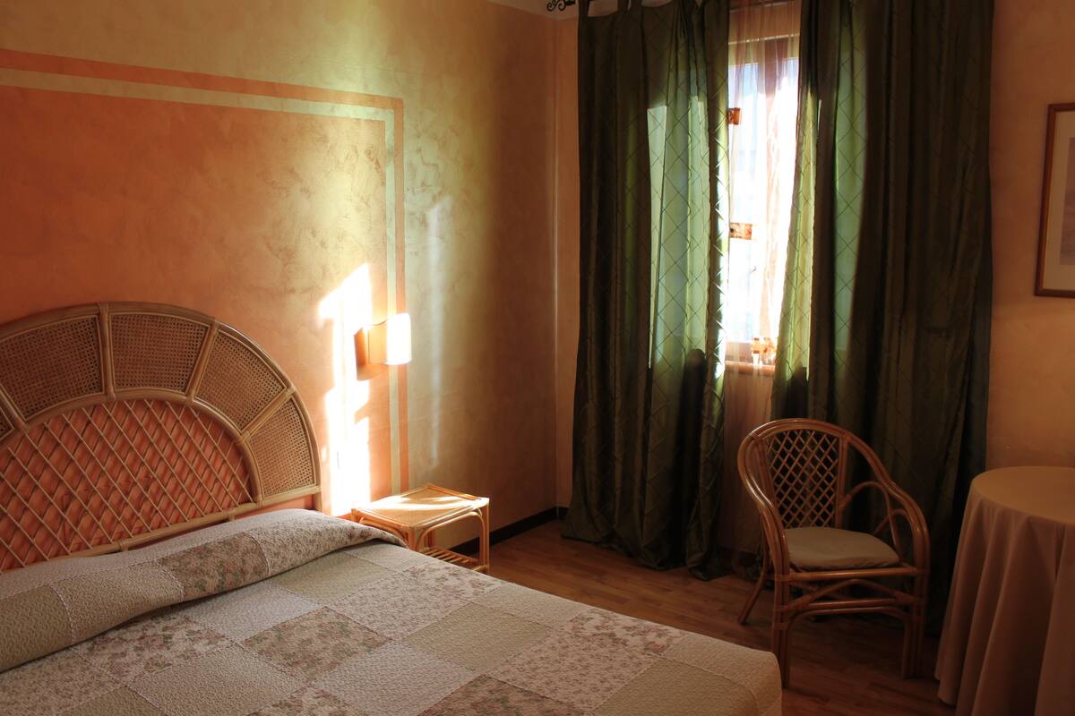 A bedroom with a bed, a chair, a small table, and a window with curtains.