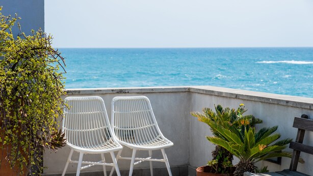 Un balcón con dos sillones blancos de mimbre frente a una vista del océano.