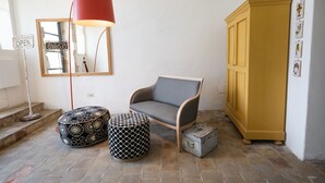 Una habitación con un sillón gris, una lámpara roja de pie, un reposapiés estampado, un pequeño cofre y un armario amarillo.