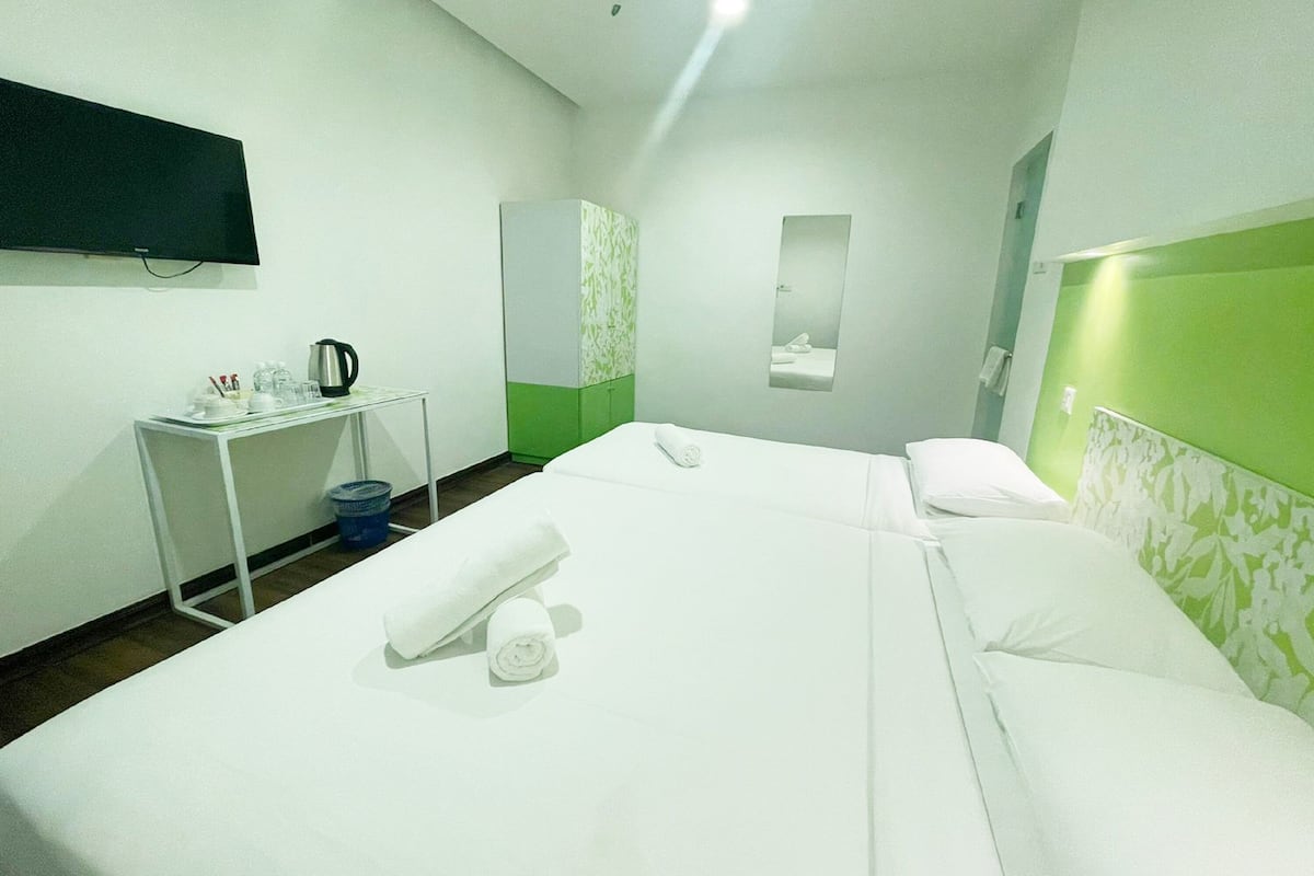 Habitación de hotel con dos camas, un escritorio con hervidor, un espejo y una pared de acento verde.