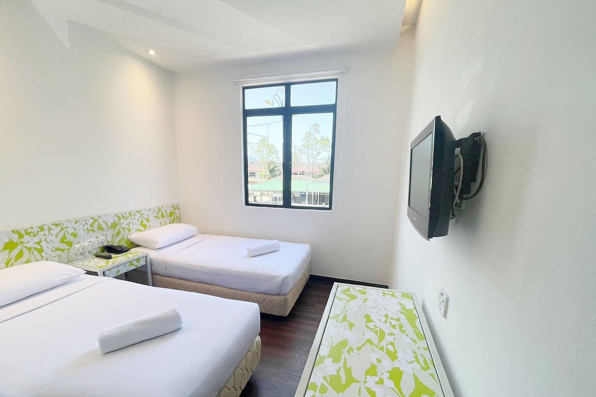 Habitación de hotel con dos camas, una mesita, televisión montada en la pared y ventana con vistas a edificios y árboles.