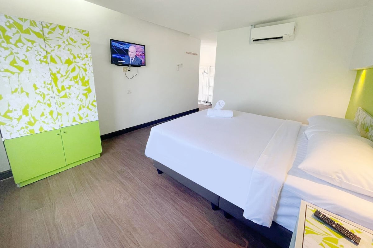 Una habitación de hotel con cama, televisión montada en la pared y aire acondicionado.