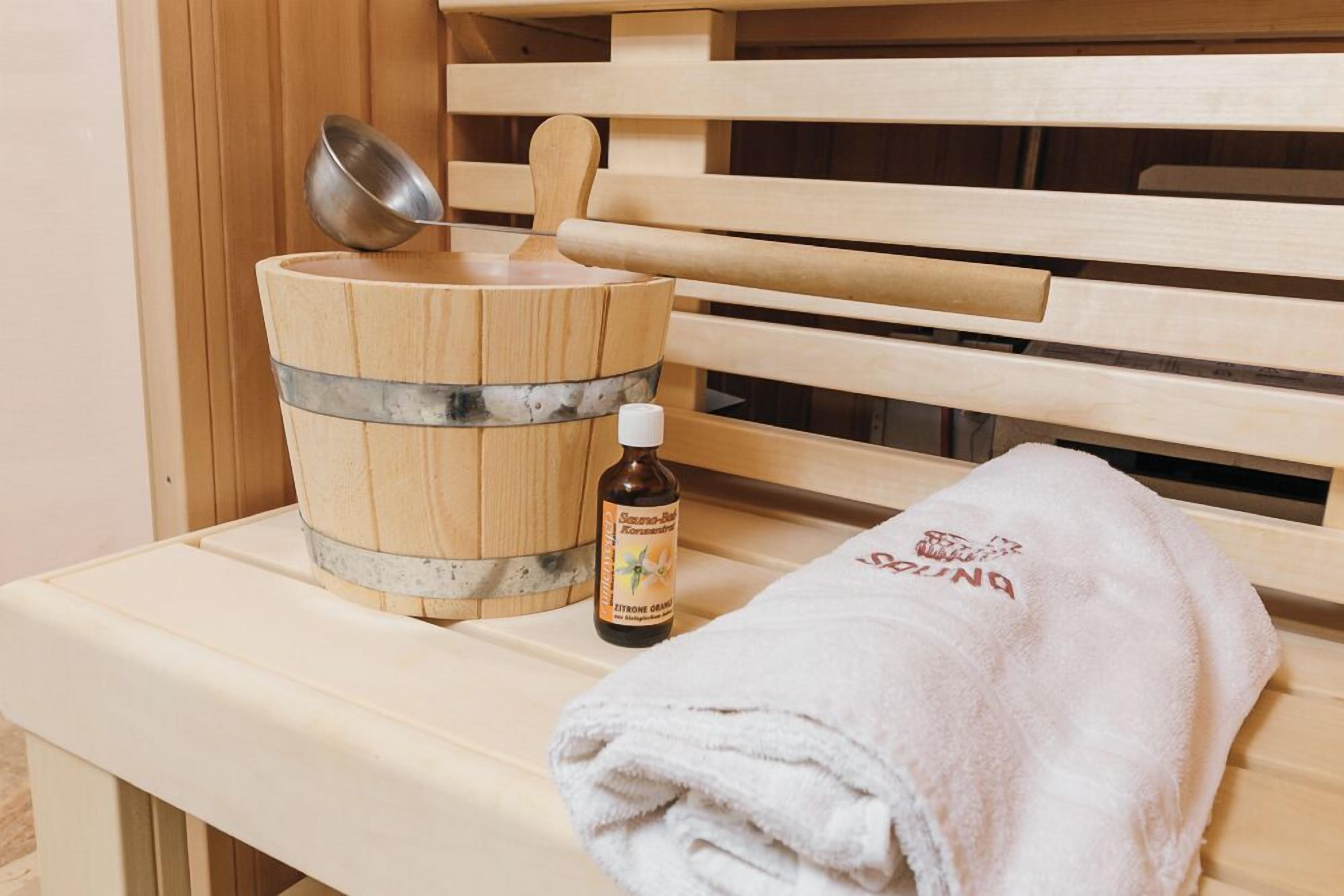 A wooden sauna bench with a metal bucket and a bottle of essential oils.