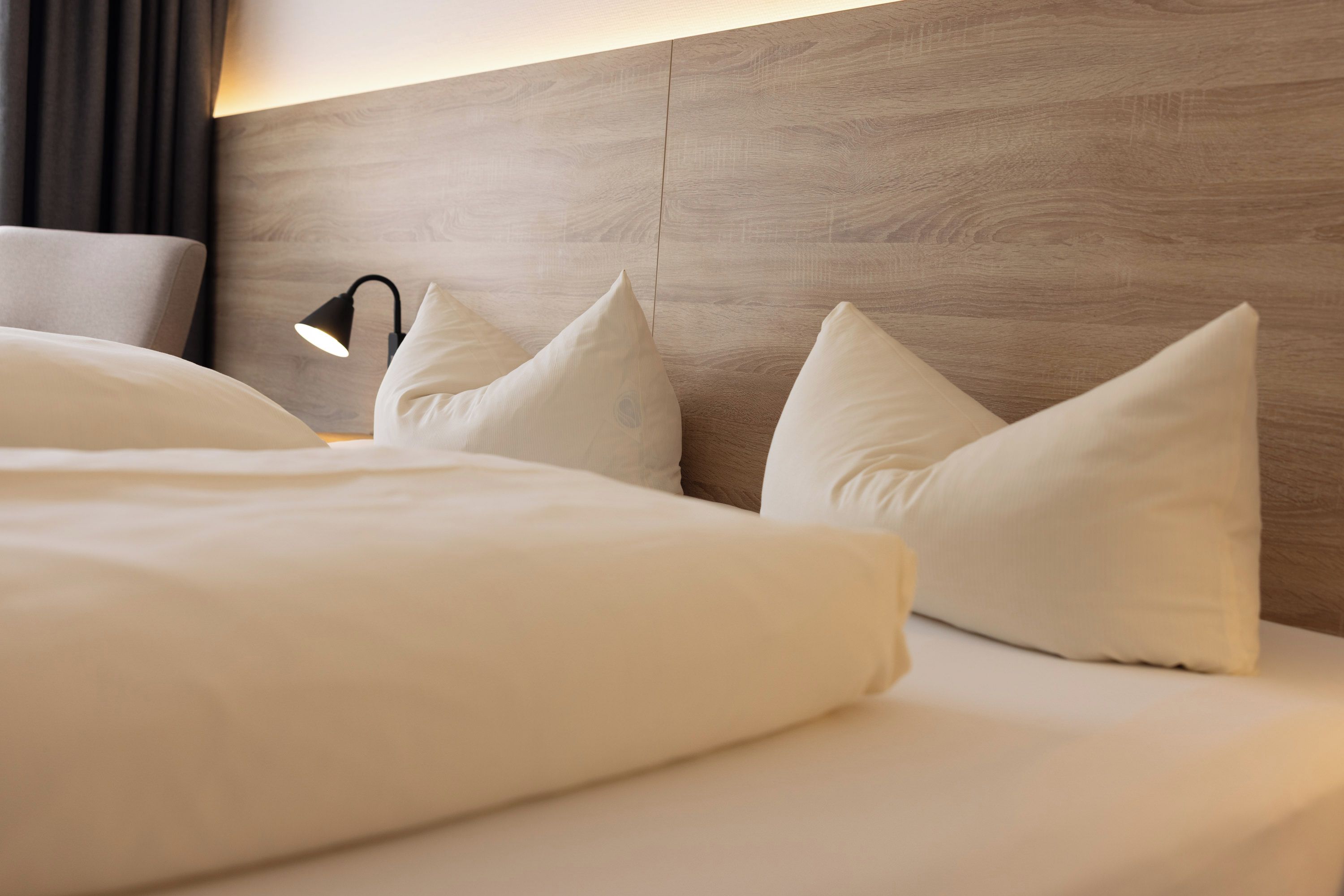 Una cama bien hecha con sábanas blancas y almohadas, una lámpara de noche y un cabecero de madera.