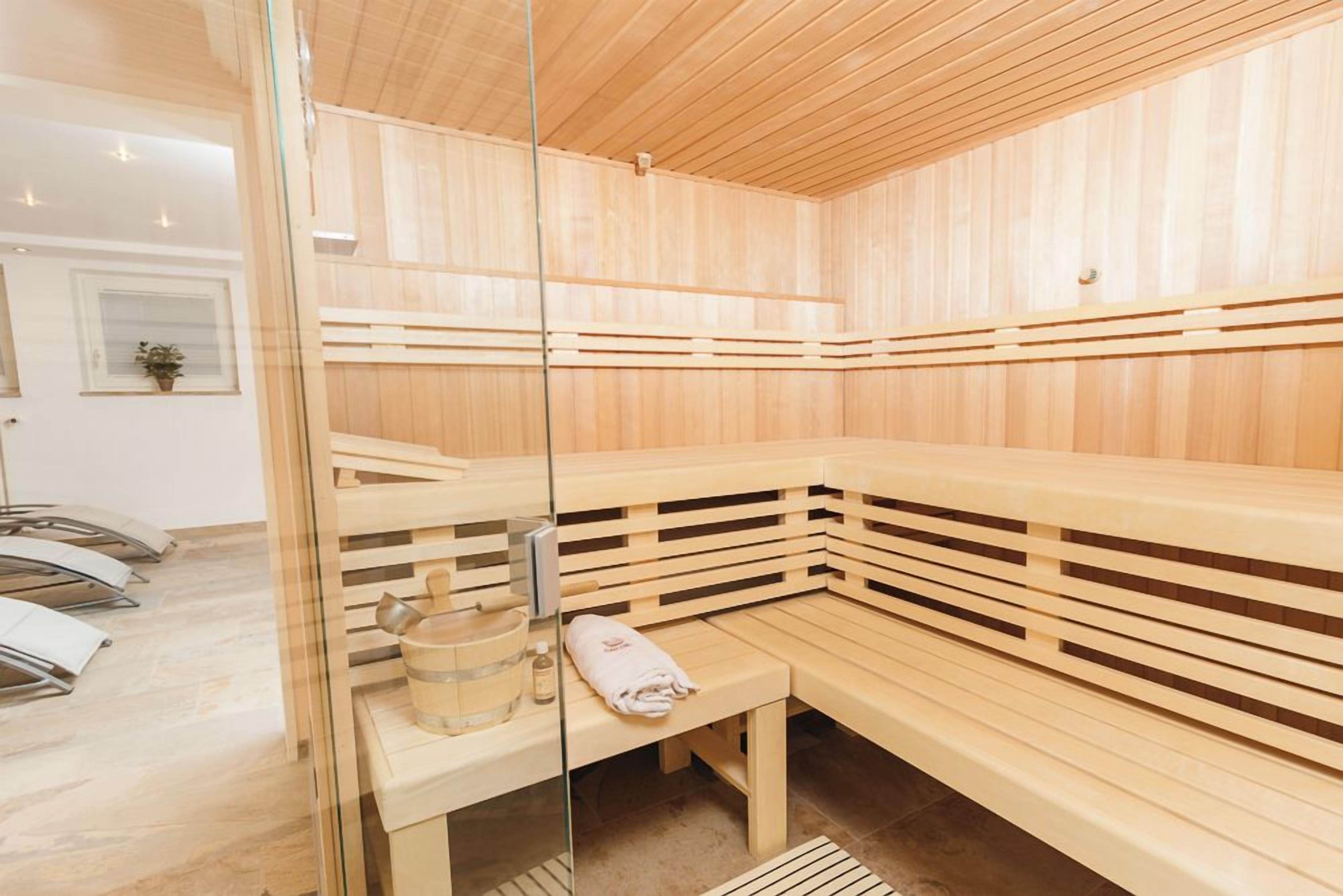 A sauna room with wooden benches, a glass partition, and a bench with a towel and a bottle.