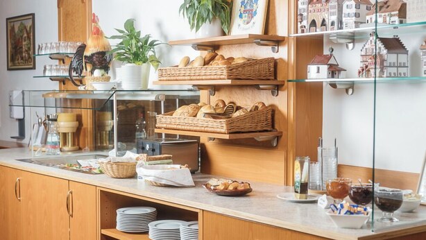 A buffet setup with wicker baskets, plates, and various food items on a counter. - Hotel Garni Brugger (Lindau)