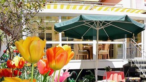 A hotel with a balcony, outdoor seating, and a garden with tulips. - Hotel Garni Brugger (Lindau)