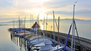 A marina with several boats docked, a pier extending into calm water, and a sunset in the background. - Hotel Garni Brugger (Lindau)