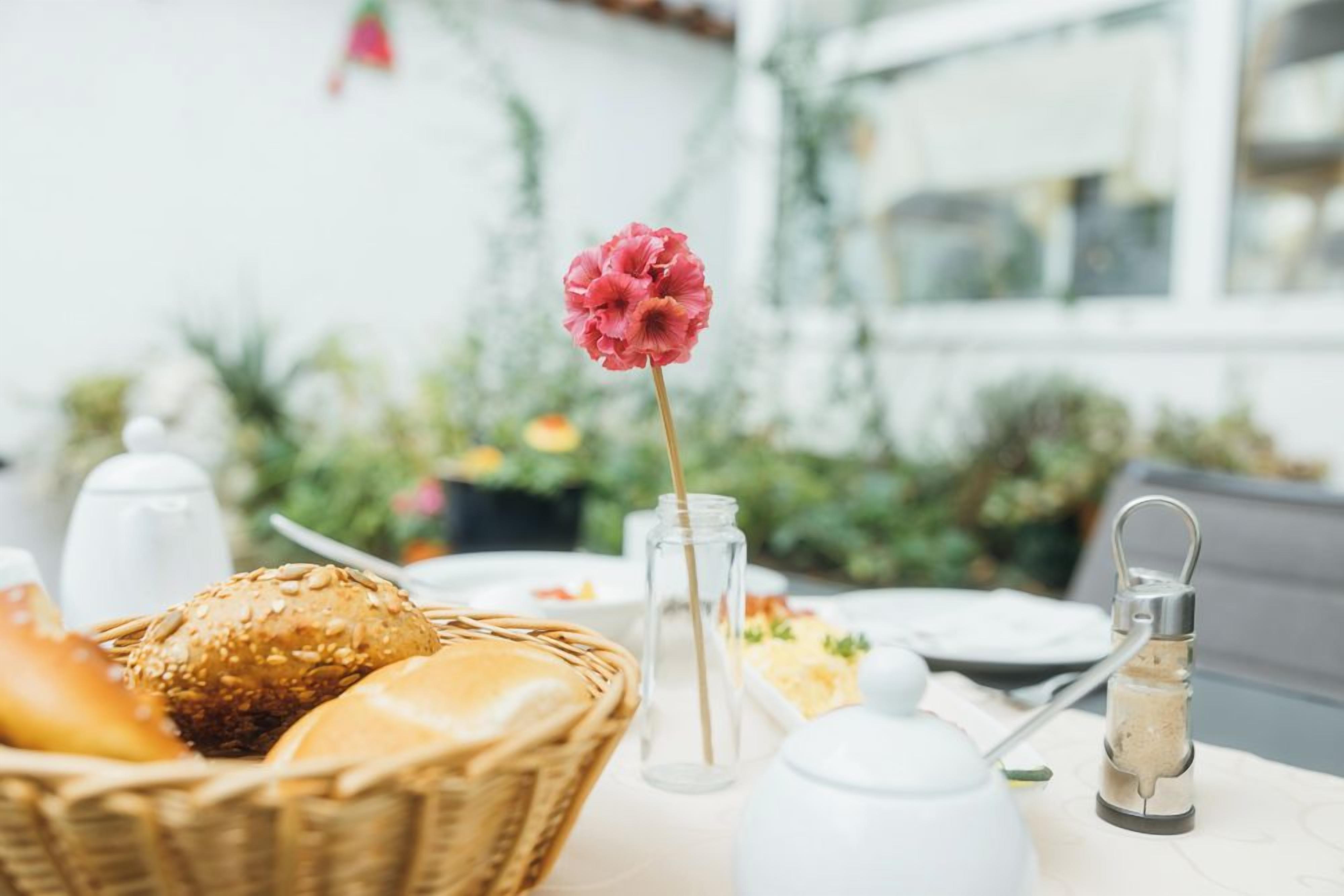 Una mesa con un cesto de pan, un tarro de cristal, un recipiente blanco y un candelabro.