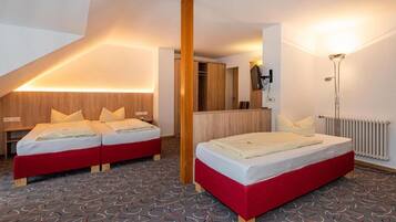 Habitación de hotel con dos camas, un armario de madera, un espejo, un escritorio y una lámpara de pie.