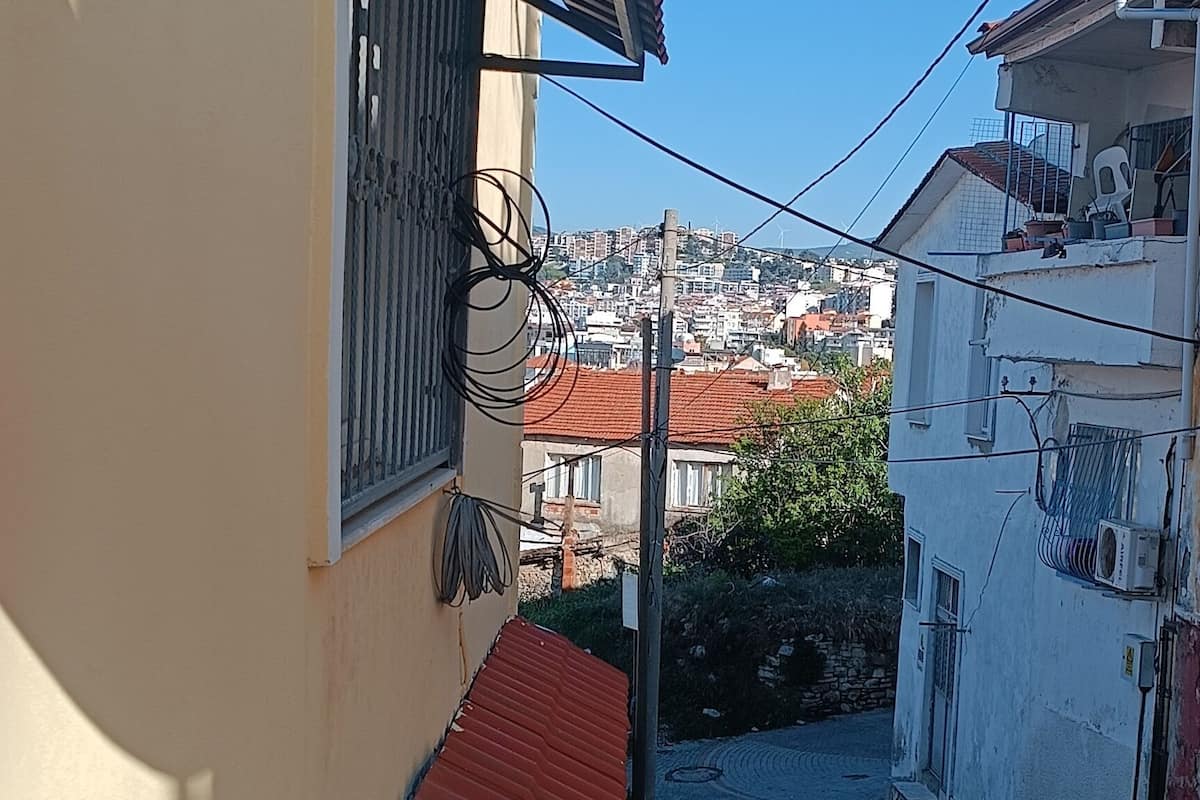 A narrow alleyway with a red roof, a white building with a window, and a clear view of the cityscape in the background.