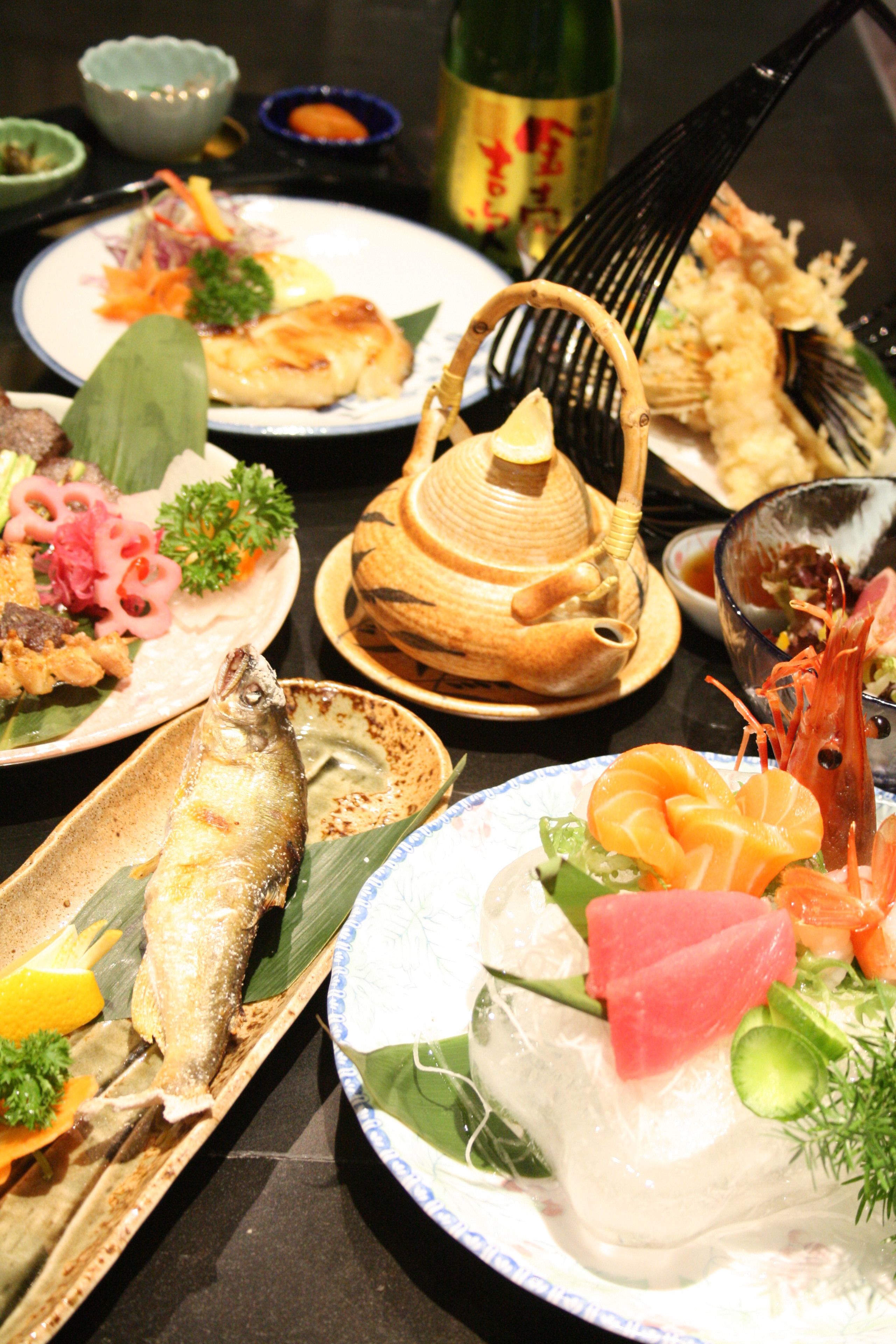 Diverse gerechten op een tafel, waaronder vis, sashimi en andere zeevruchten.