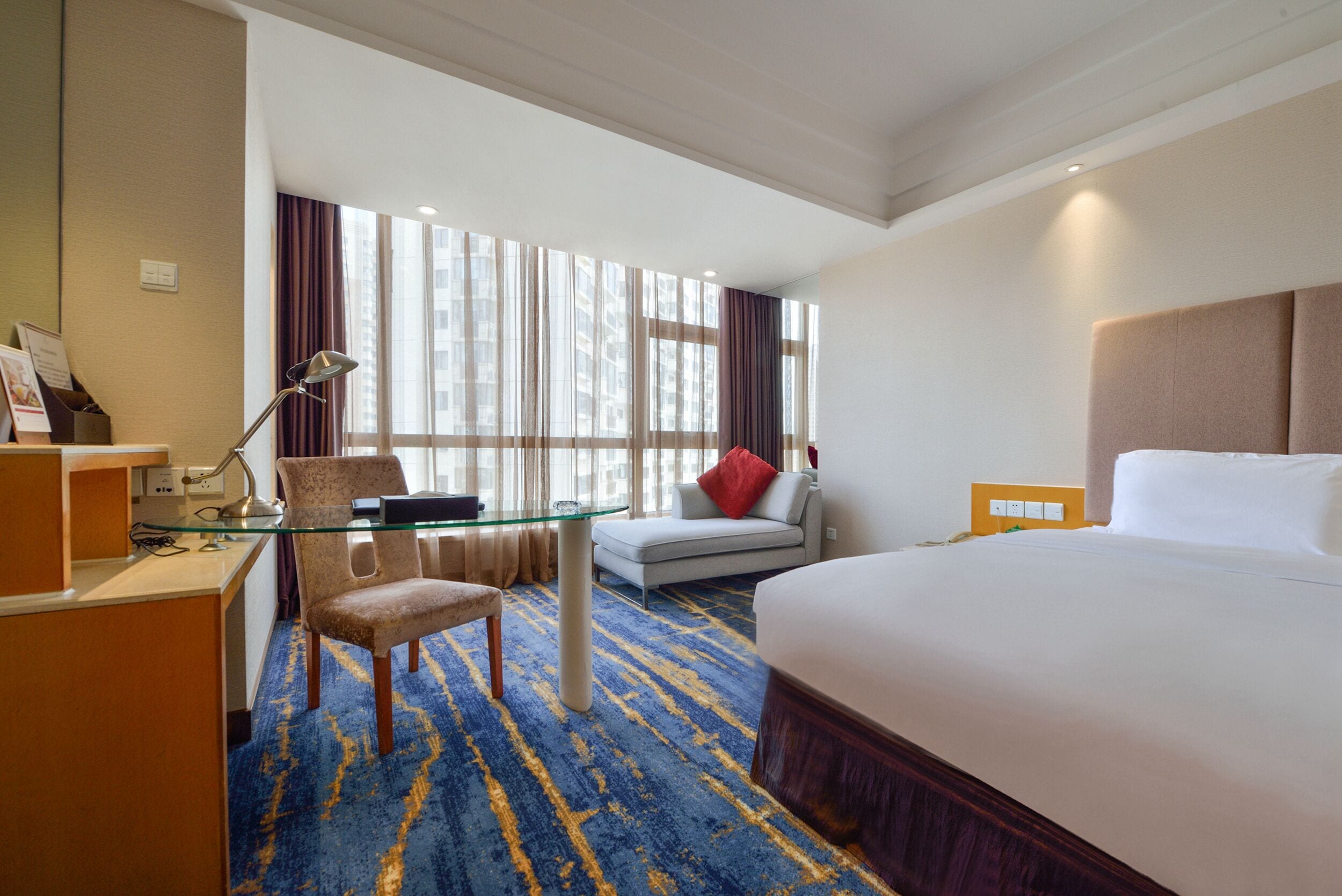 Habitación de hotel con una cama grande, un escritorio con silla, una mesita de vidrio y un sofá.
