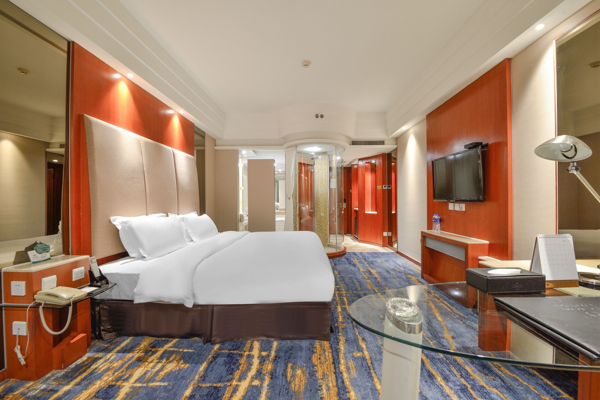 A hotel room with a large bed, a desk with a computer, a TV, and a glass coffee table.
