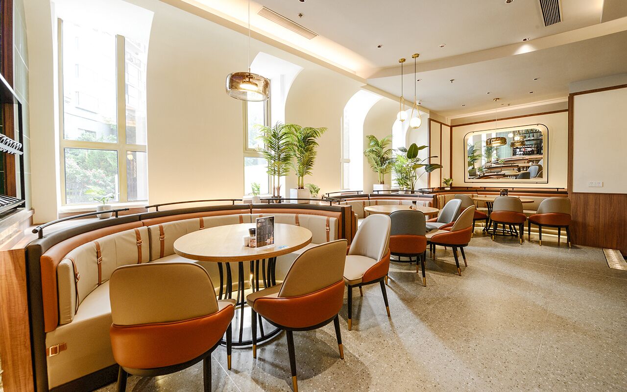 A modern interior with a curved seating area, round tables, and potted plants.