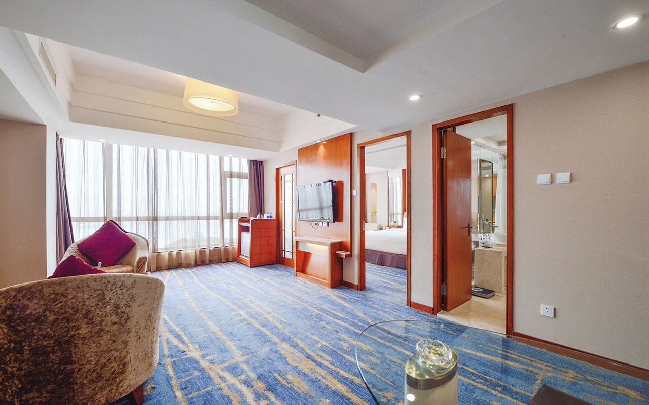 Una habitación de hotel con un ventanal grande, una cama, un escritorio, una silla y un televisor.