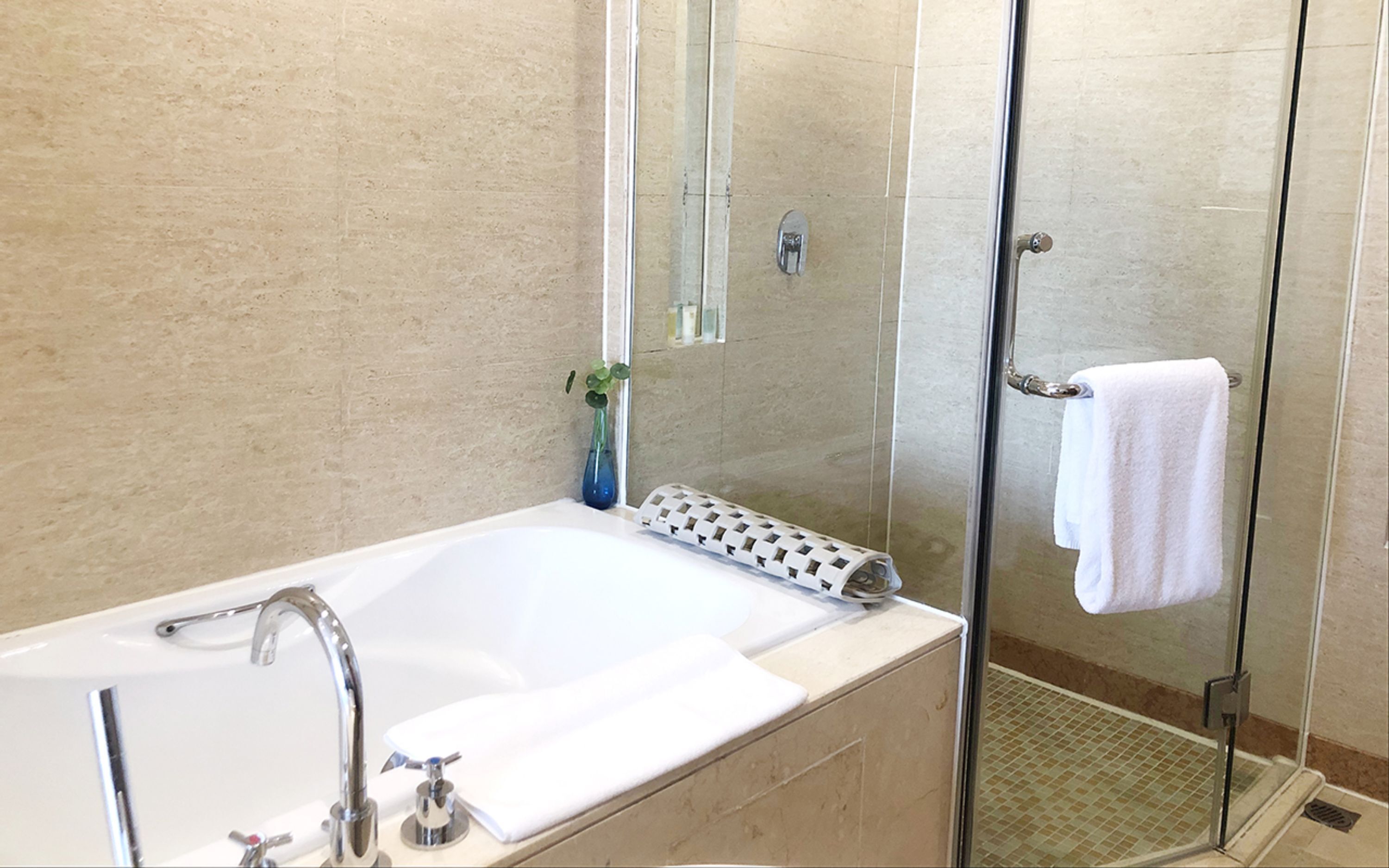 Une salle de bain moderne avec une douche à l’italienne en verre, une baignoire blanche et un petit vase avec une plante.