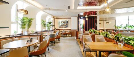 A modern restaurant with round tables and cushioned booths, featuring a central dining area and a bar.