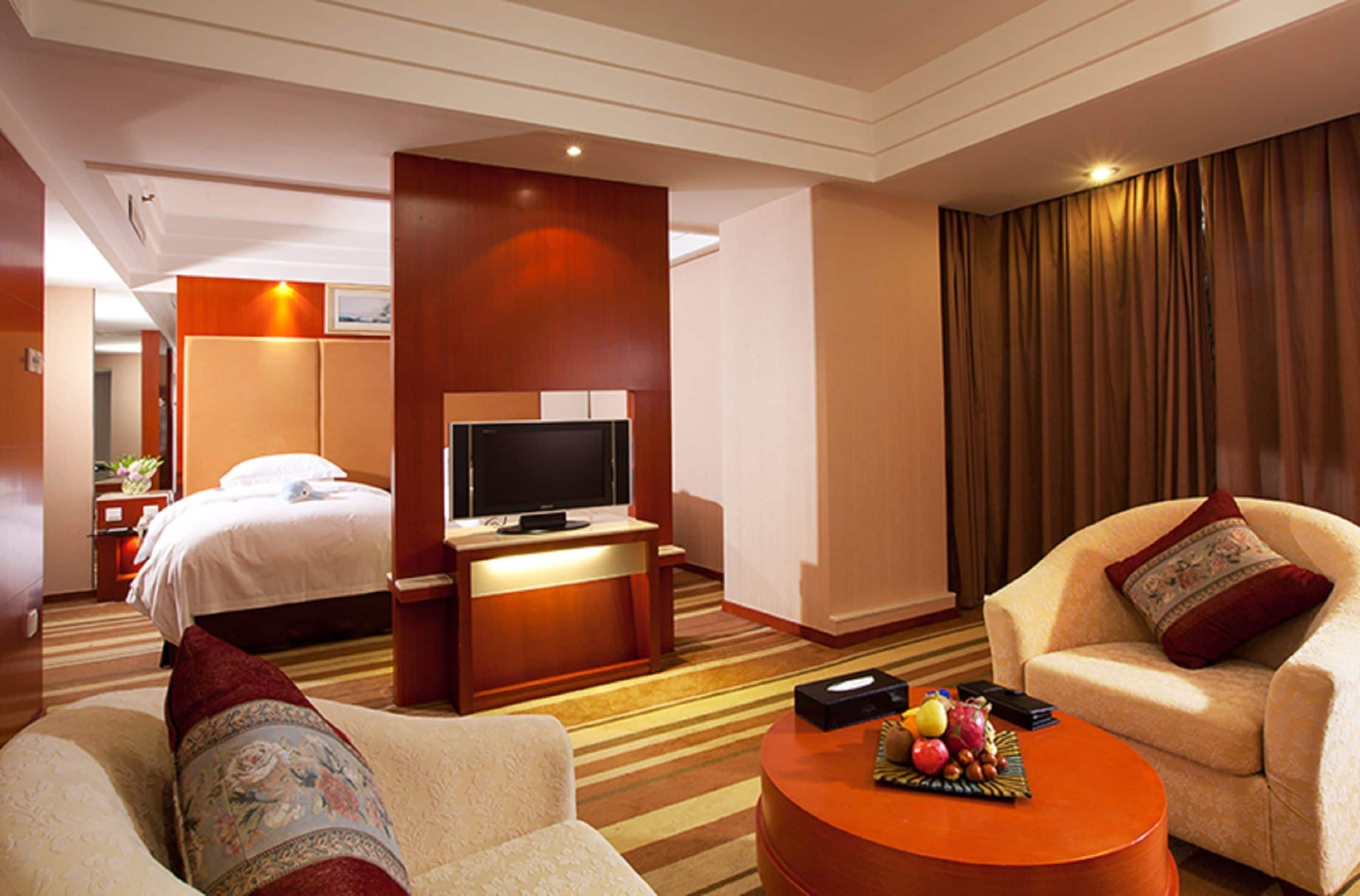 Habitación de hotel con una cama, televisor, una mesita de centro con fruta y un sofá.