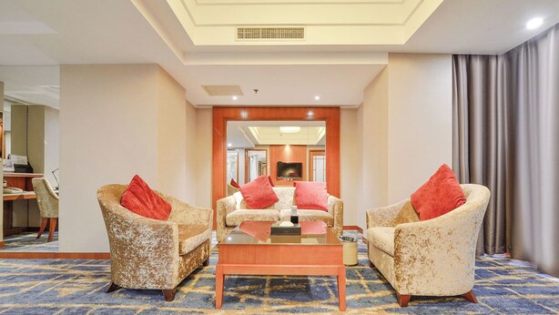 Habitación de hotel con sala de estar que incluye dos sillones con cojines rojos, una mesa de centro de vidrio y un televisor de pantalla plana montado en la pared.