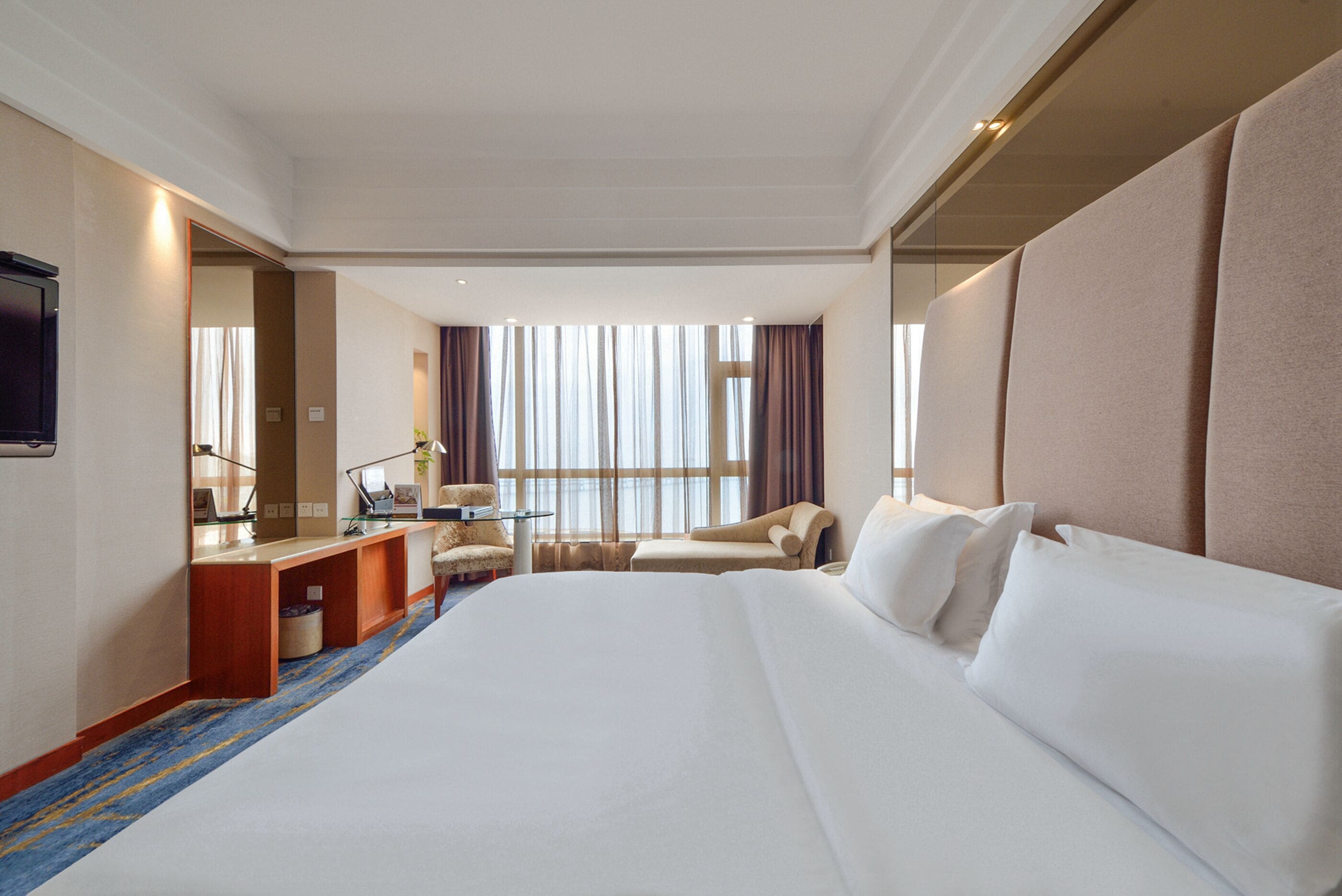 A hotel room with a large bed, a desk, a chair, and a window with curtains.