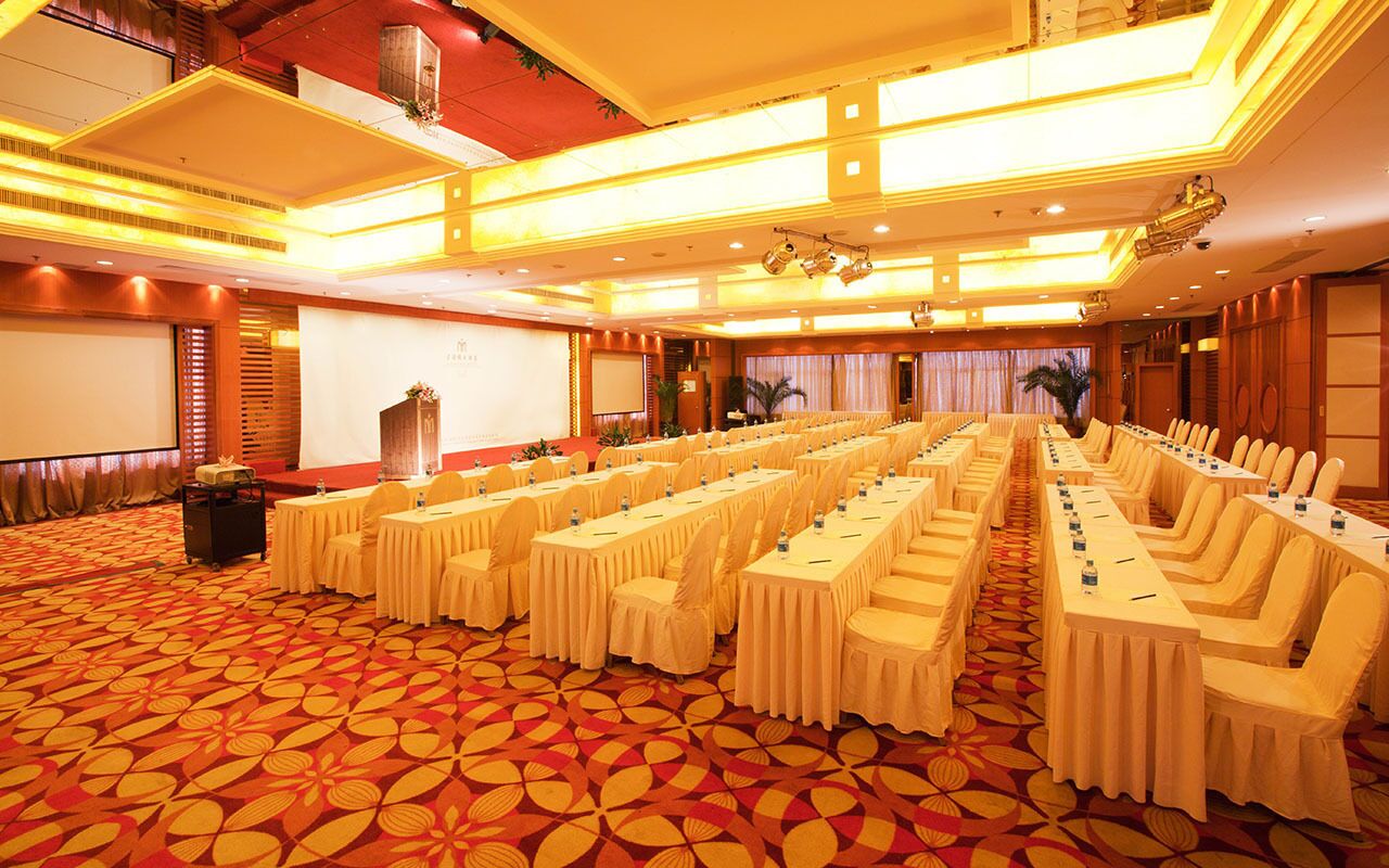 A conference room with rows of tables and chairs, a projector screen, and a carpeted floor.