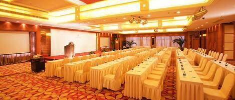 A conference room with rows of tables and chairs, a projector screen, and a carpeted floor.