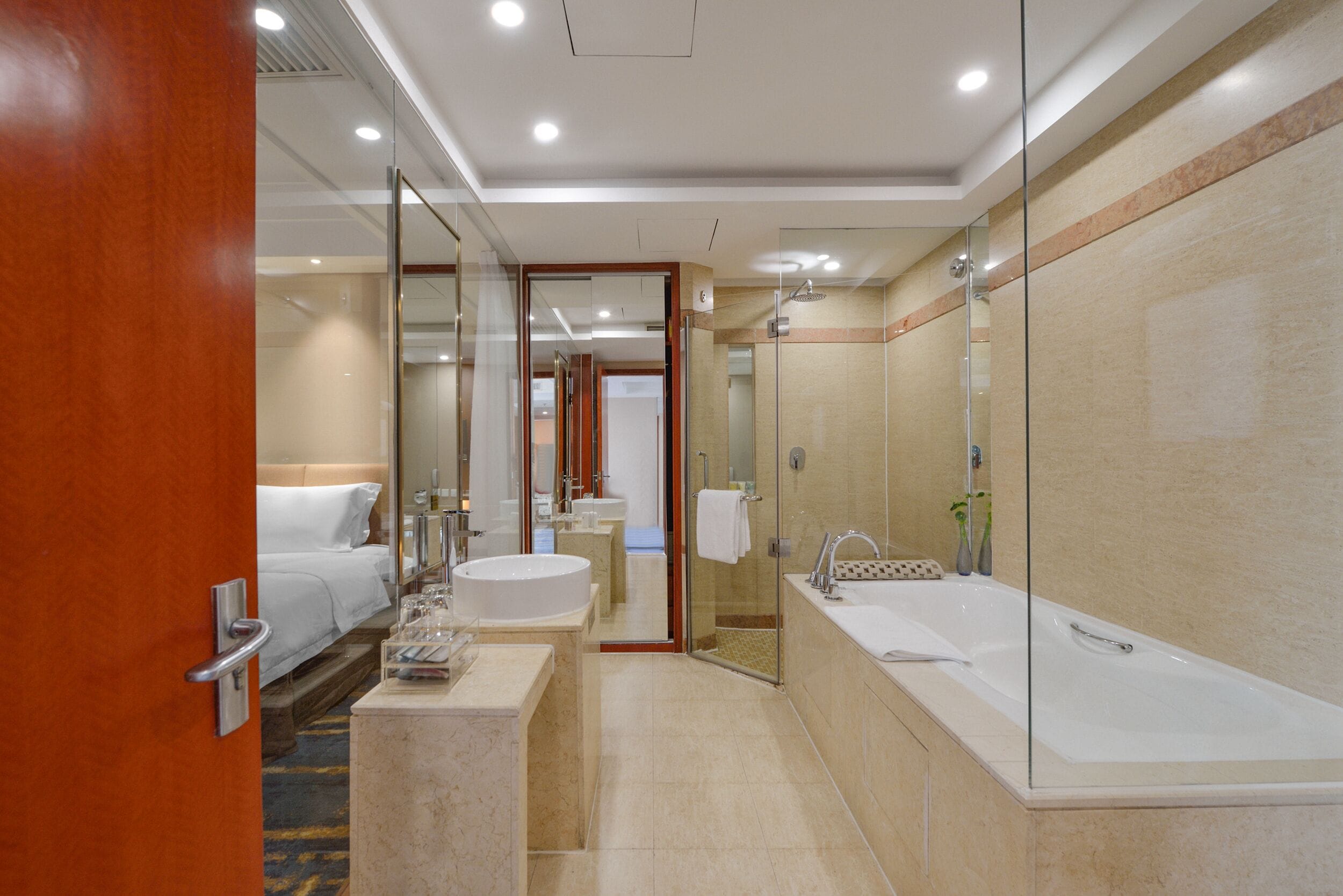Un baño de hotel moderno con una bañera grande, zona de ducha separada y un vestidor amplio con puertas de cristal.