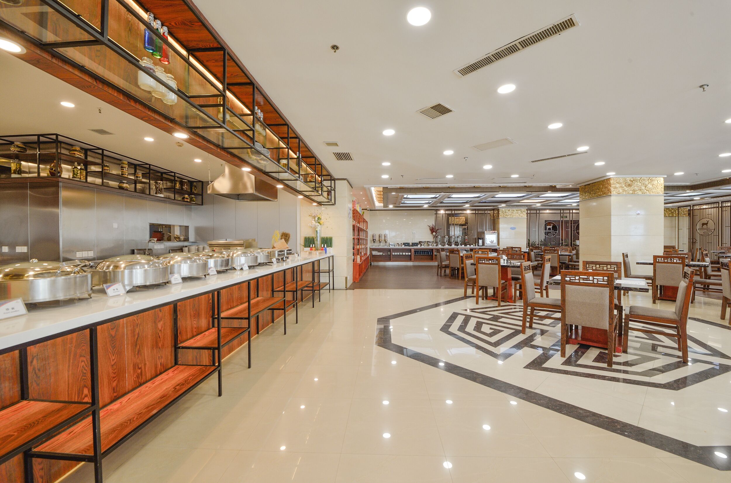 A spacious cafeteria with long wooden benches and tables, equipped with stainless steel food containers.