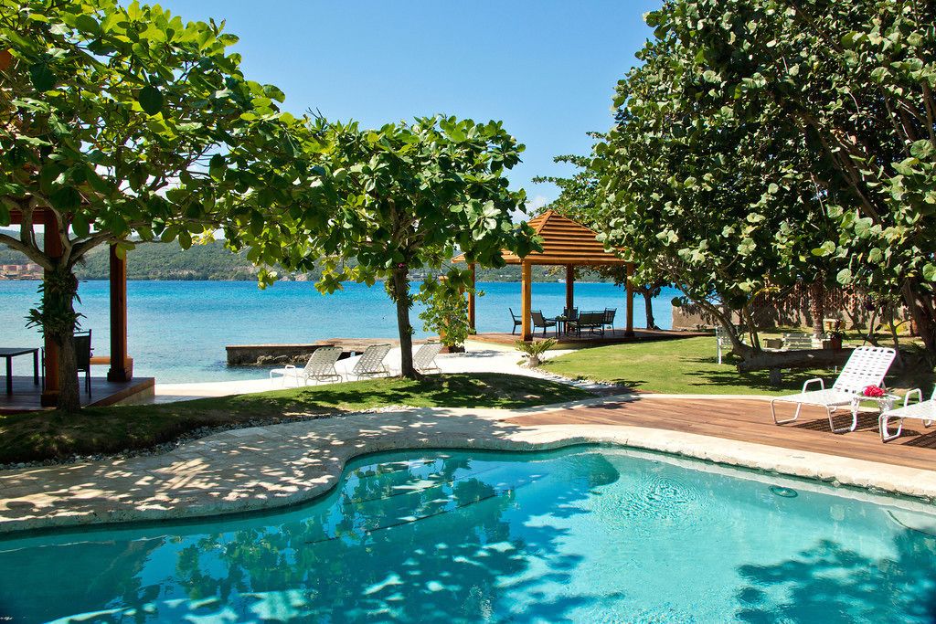 Uma área de piscina com espreguiçadeiras, um gazebo e vista para o mar.
