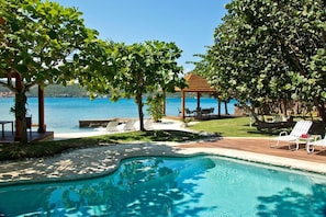 A pool area with lounge chairs, a gazebo, and a view of the sea.