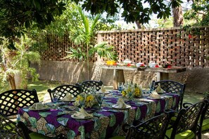 An outdoor dining area with a brick wall, green chairs, and a table set with plates, napkins, and flowers.