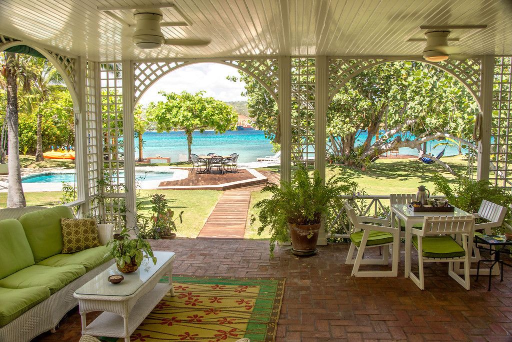 Un patio techado con vistas a una piscina y al océano, amueblado con un sofá, una mesa y sillas.