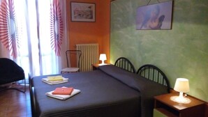 A hotel room with a bed, two bedside tables with lamps, a chair, a radiator, and a window with curtains. - Soggiorno Petrarca (Florence)