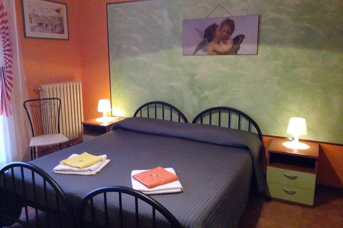 A hotel room with a bed, two bedside tables with lamps, a chair, and a radiator.