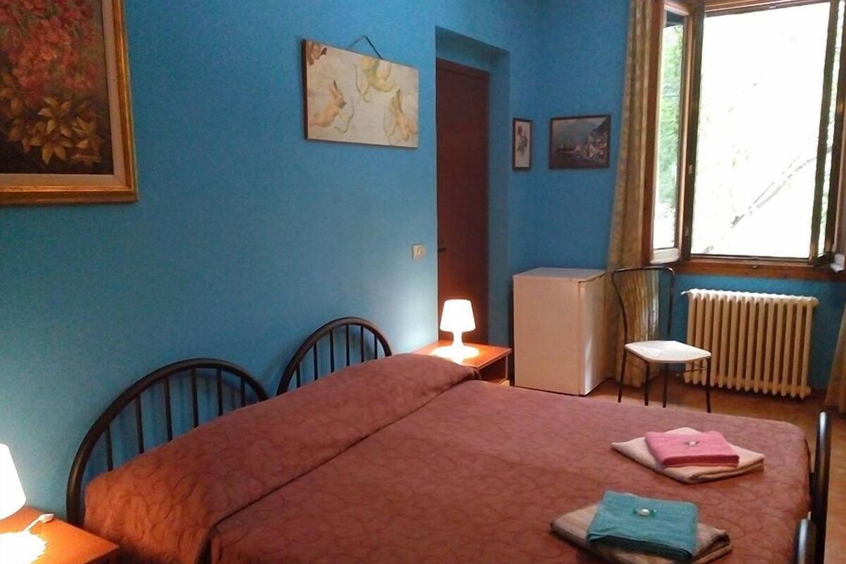 A bedroom with a bed, a desk with a lamp, a radiator, and a window with curtains.