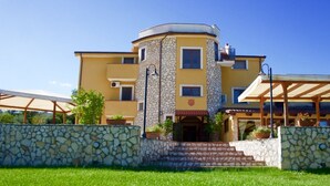 A multi-story building with a stone facade, a central entrance with steps, and a covered outdoor area.