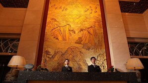 Una recepción con un gran mural de un paisaje montañoso y dos personas detrás.