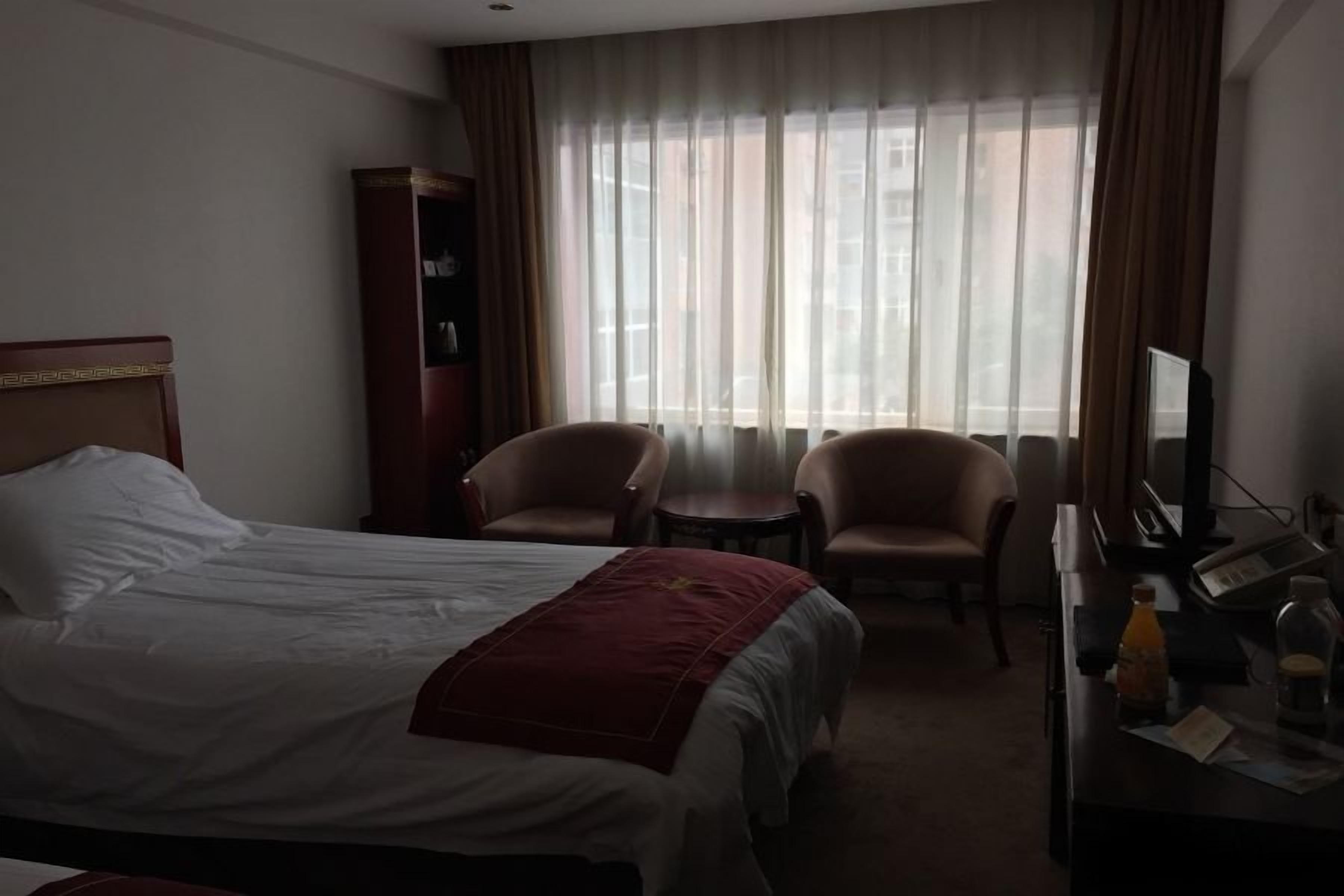 A hotel room with a bed, two armchairs, a desk with a computer, and a television.
