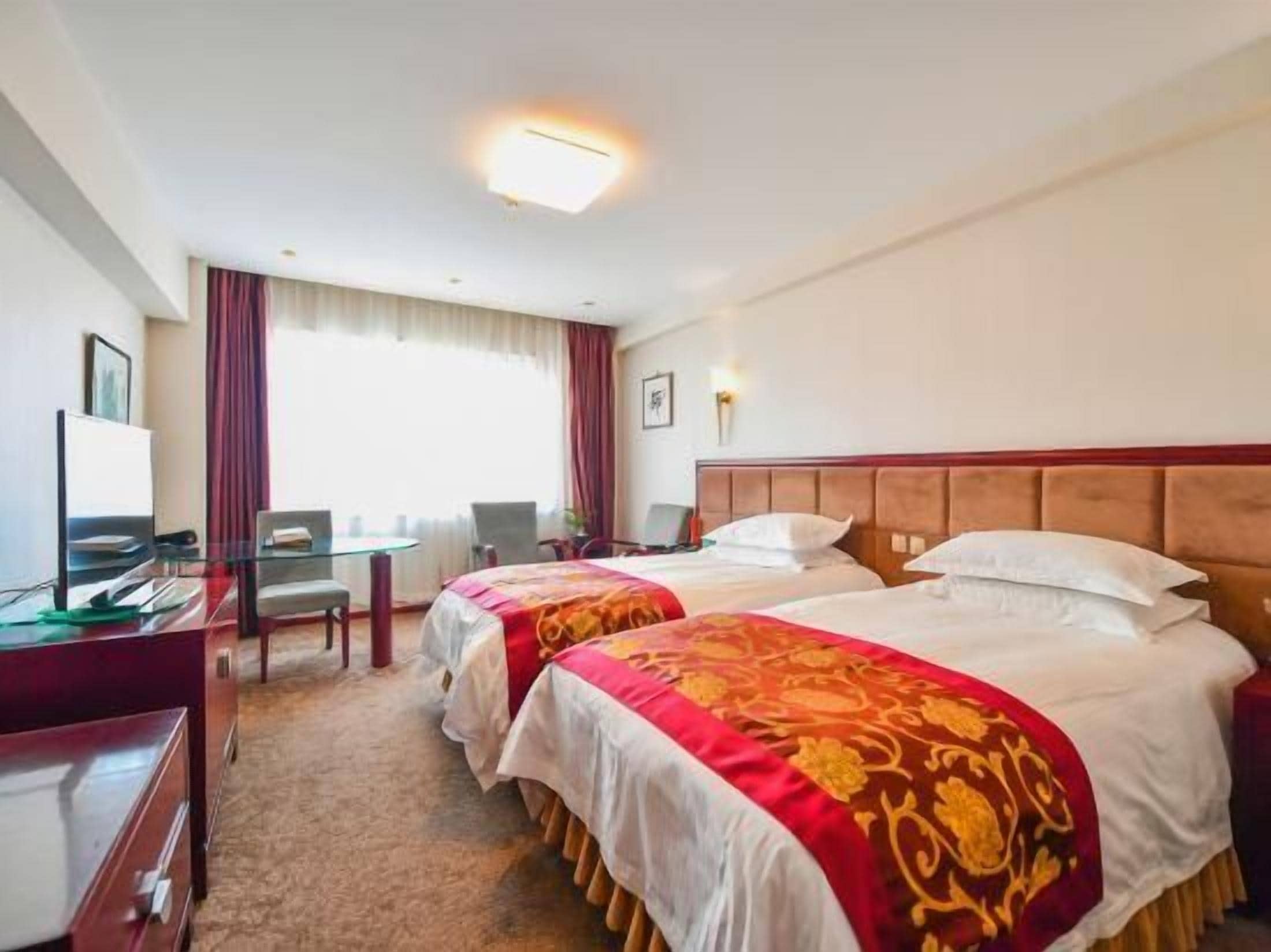 Een hotelkamer met twee bedden, een bureau, een stoel, een televisie en een raam met gordijnen.